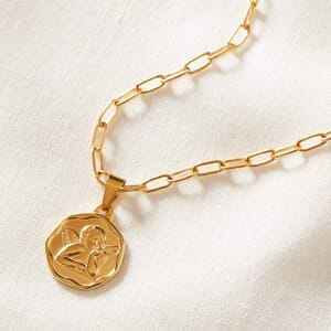 Close up photo of a Angel coin gold stainless steel necklace lying on a cream cloth