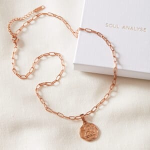 Angel coin rose gold necklace lying on a cream cloth also on top of a soul analyse box