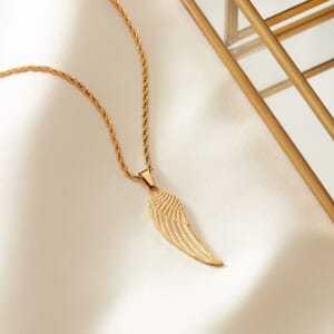 Angel wing Rose Gold stainless steel necklace placed on a cream cloth with artefact in the corner