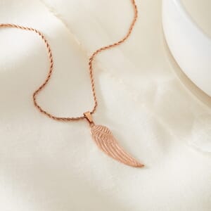 Angel wing Rose Gold stainless steel necklace placed on a cream cloth