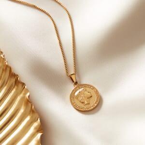 Audrey Hepburn Gold plated stainless steel necklace placed on a cream cloth alongside a gold plate
