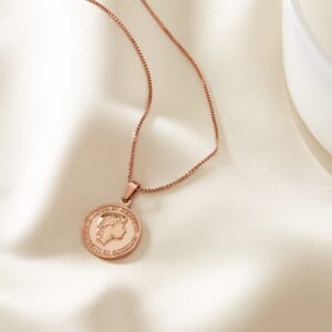 Audrey Hepburn ' nothing is impossible' rose gold stainless steel necklace lying on a cream cloth