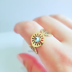 A gold plated sterling silver Turkish eye ring with blue stone worn on index finger with a soul analyse box in the background.