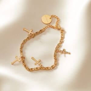 Cross charm Gold stainless steel bracelet placed on a cream cloth spread out