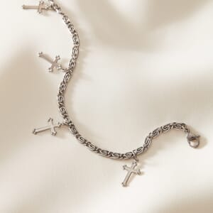 Cross charm silver stainless steel bracelet placed on a cream cloth spread out
