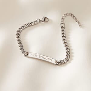 I AM ENOUGH curb stainless steel silver bracelet placed on a cream cloth