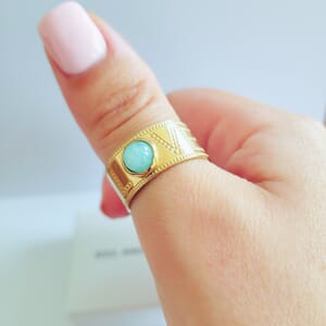 A gold plated Hug ring with turquoise stone worn on thumb