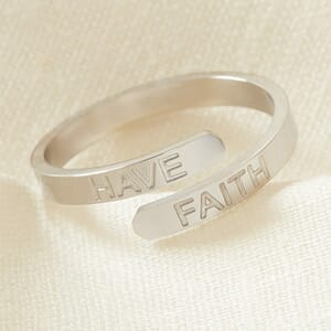 The HAVE FAITH affirmation stainless steel adjustable ring placed on a cream cloth 