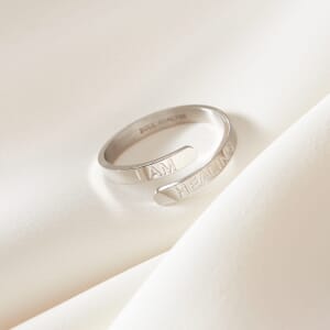 a I am healing stainless steel silver adjustable ring placed on a cream cloth