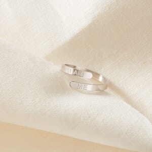 The I AM ME affirmation stainless steel adjustable ring placed on a cream cloth 