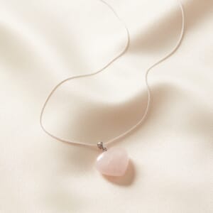 Rose quartz heart pendant necklace placed on a cream cloth