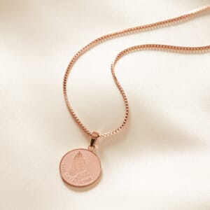 close up photo of serenity rose gold stainless steel necklace placed on a cream shee
