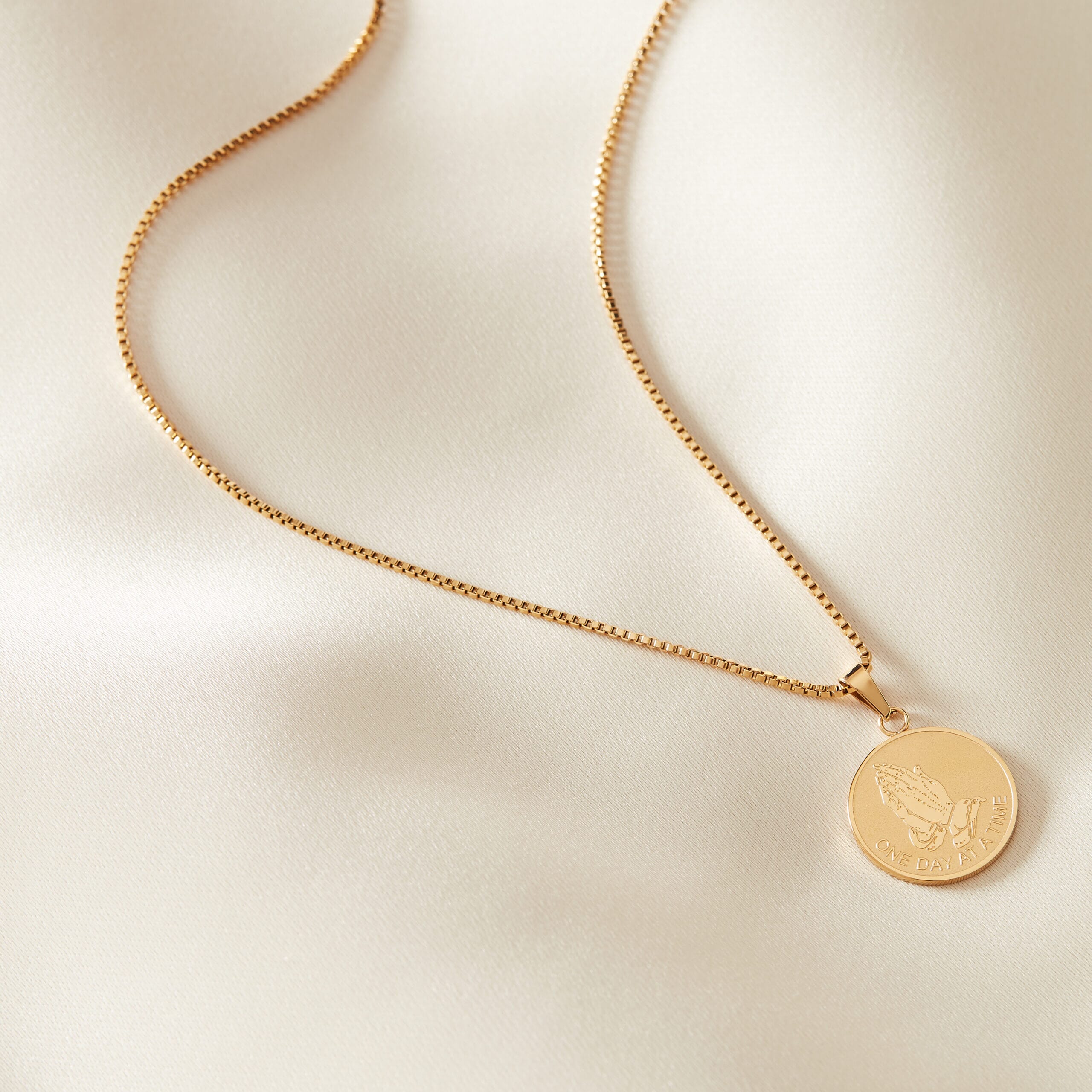 serenity gold stainless steel necklace placed on a cream sheet