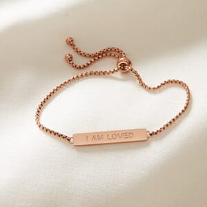 I AM LOVED metal rose gold stainless steel rope bracelet placed on a cream cloth