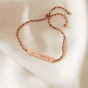 I AM STRONG metal rose gold stainless steel rope bracelet placed on a cream cloth