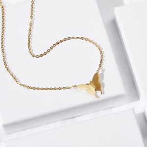 a butterfly gold necklace made from stainless steel lying on a couple of soul analyse boxes