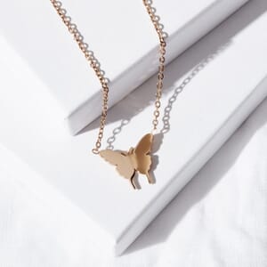 a butterfly rose gold necklace made from stainless steel lying on a couple of soul analyse boxes