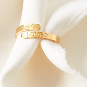 I AM LOVED affirmation adjustable stainless steel gold ring worn by a cream cloth