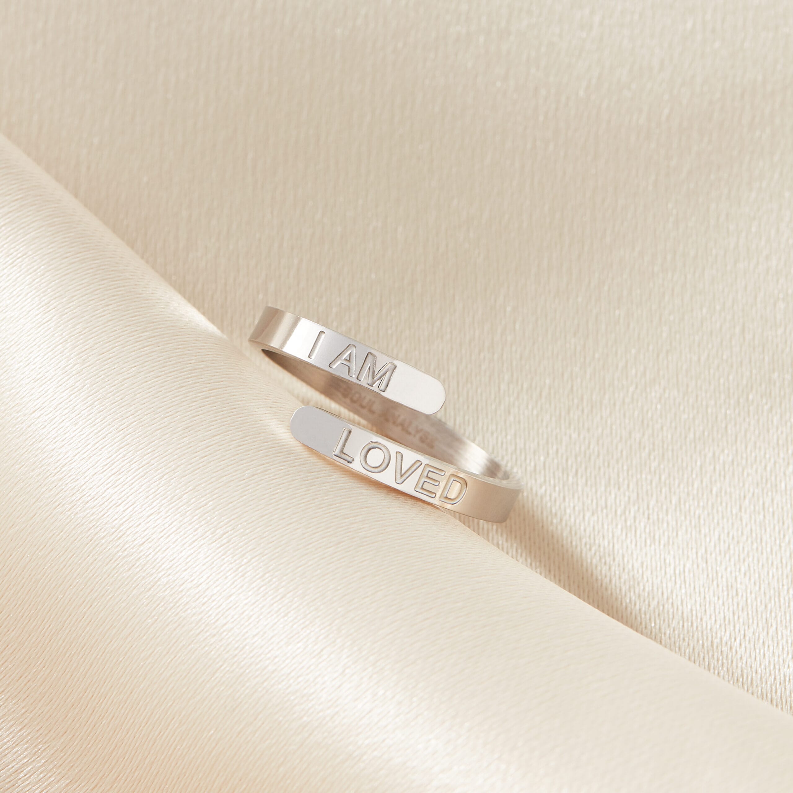 I am loved stainless steel adjustable silver ring resting on a cream sheet