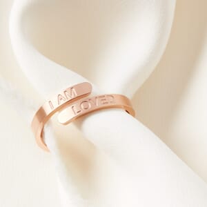I AM LOVED affirmation adjustable stainless steel rose gold ring worn by a cream cloth